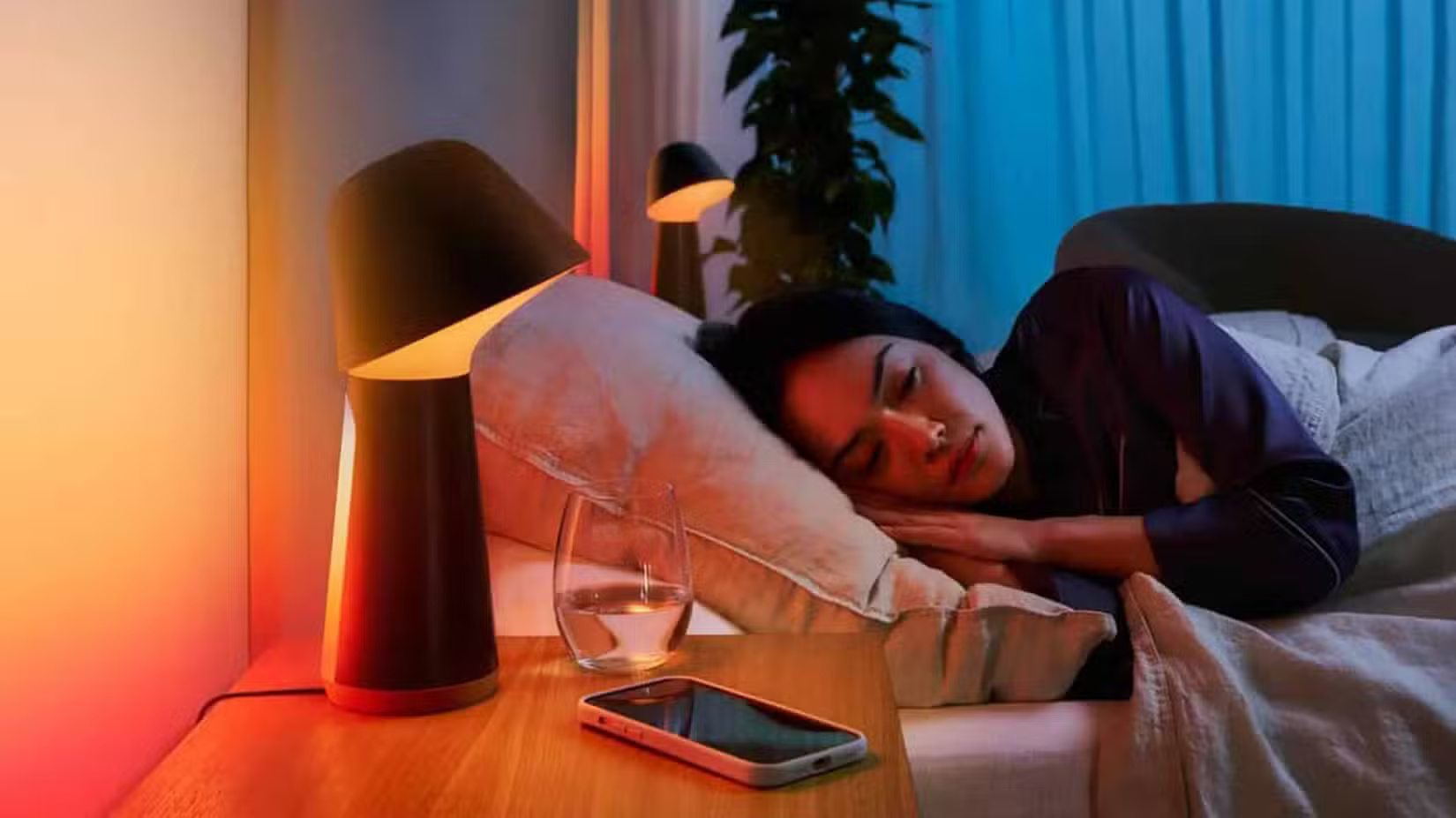 a-woman-sleeping-in-a-bed-next-to-a-smart-lamp-and-a-smartphone كيف تقاوم الرغبة في شراء هاتف جديد باستخدام نصائح عملية