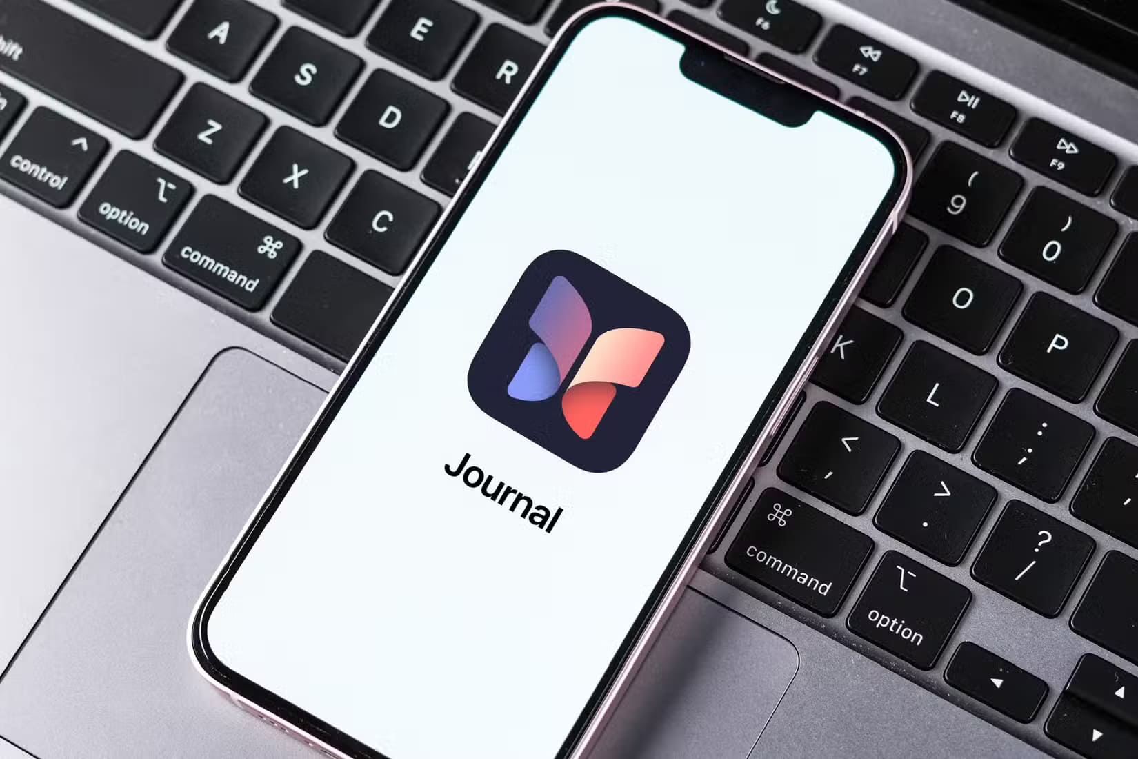 apple-s-journal-app-on-an-iphone-screen-on-a-macbook-keyboard أخطاء شائعة في استخدام الآيفون تؤثر على أدائه وكيفية تجنبها